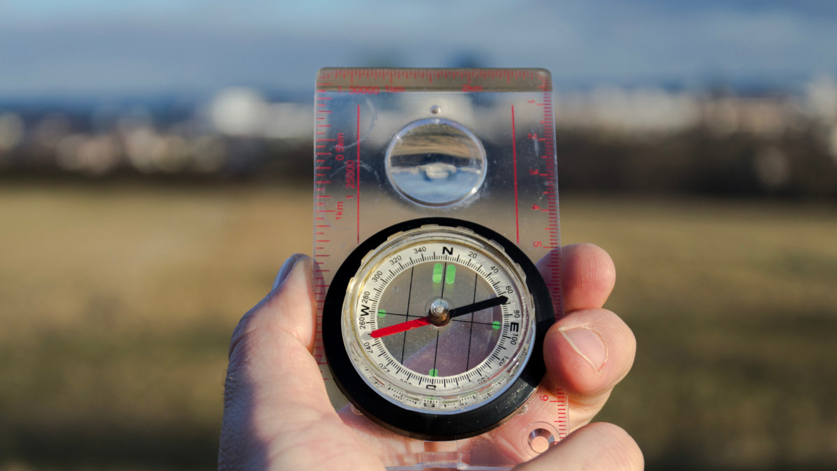 hand-holding-glass-compass-nature-in-backgroun